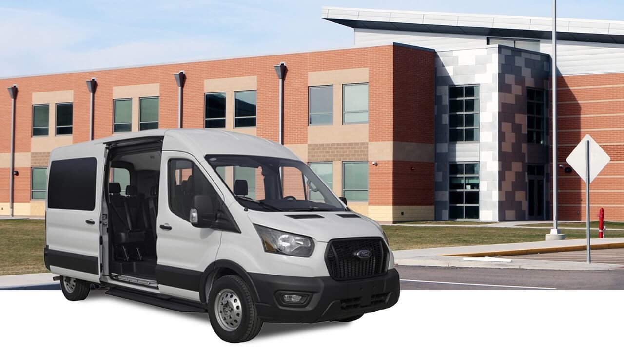 A white passenger van is parked in front of a modern brick and glass building with multiple windows and a crosswalk nearby.