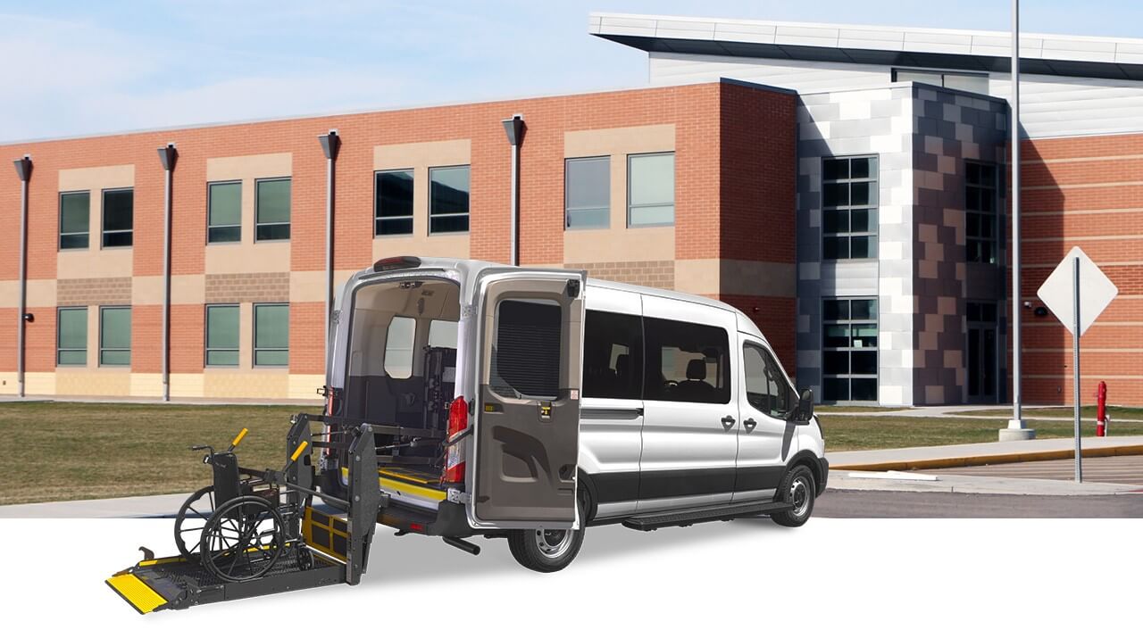 A van with a wheelchair accessibility ramp extended is parked outside a modern brick building.